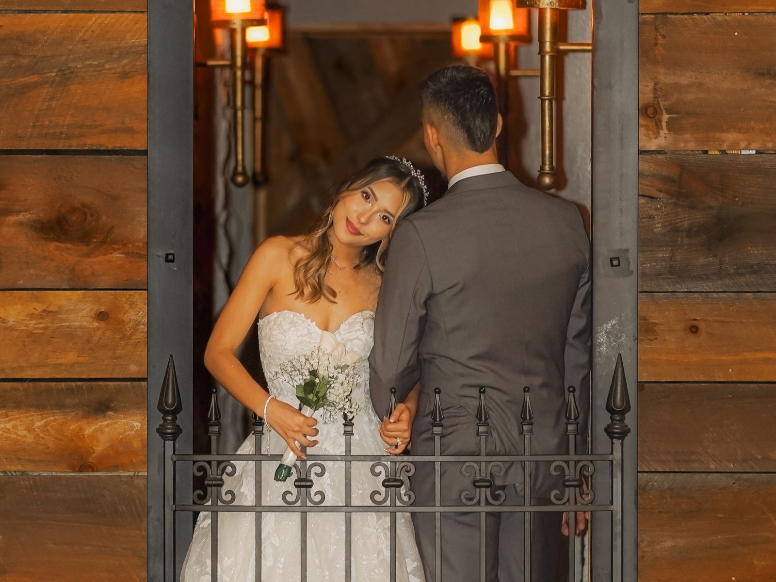 A bride and groom in a lit doorway at the Castle, framed by an ornamental iron gate, with reclaimed timber walls either side