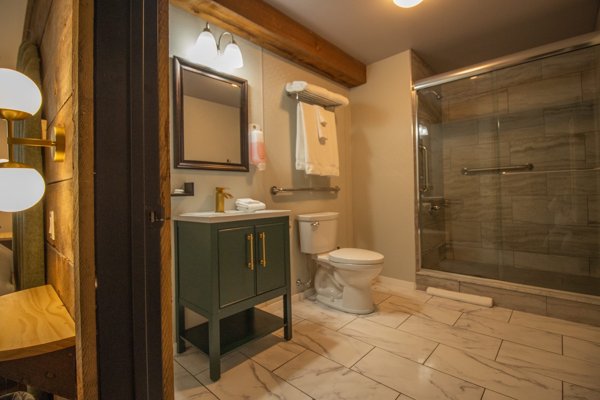 A bathroom with a green vanity, a toilet with a grab bar and a glass shower with a grab bar inside