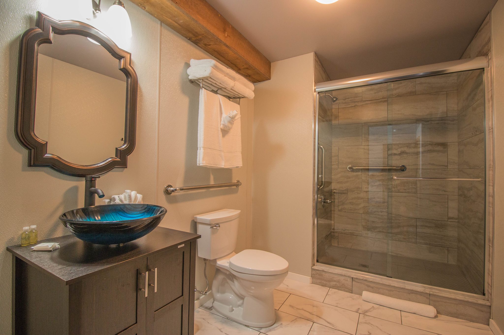 A bathroom with a glass bowl sink on a dark vanity and a glass-walled shower
