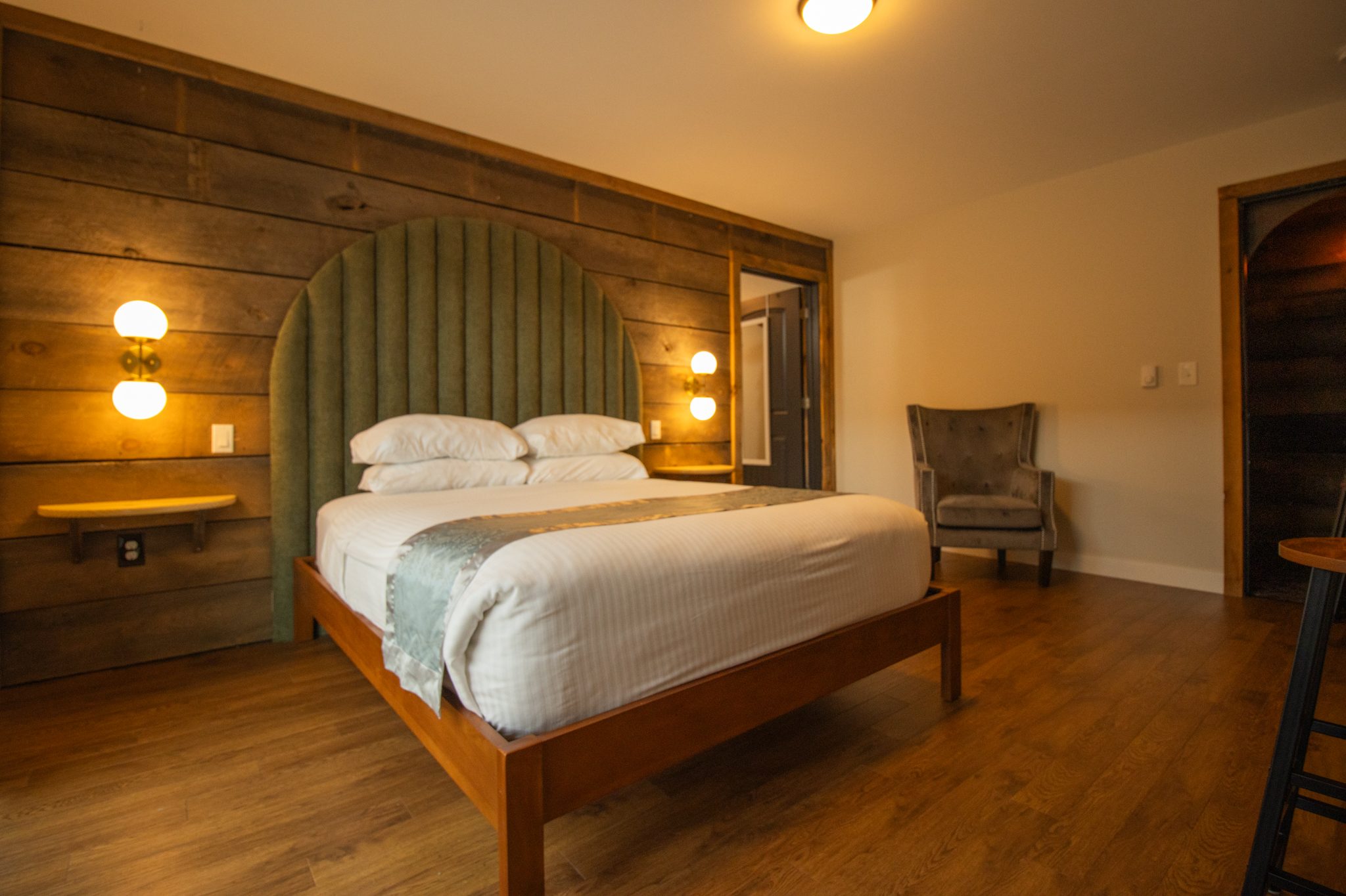 A larger queen bedroom with an arched headboard, an armchair and a timber wall
