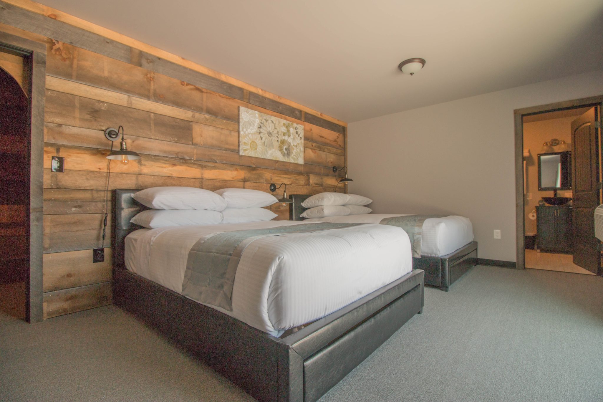 A bedroom with two queen beds against a reclaimed-timber wall