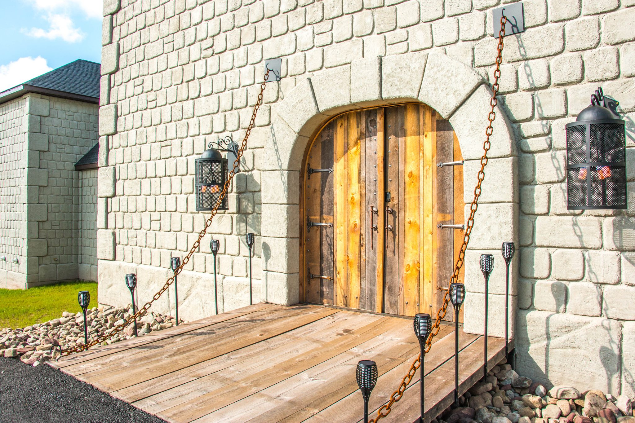 The Castle's arched timber front doors behind a timber drawbridge deck lit by torches