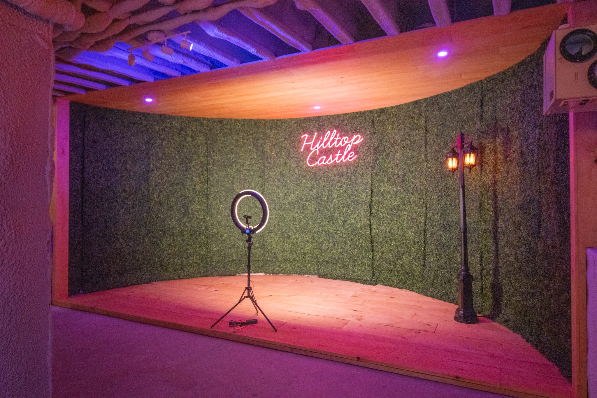 The selfie stage: a green hedge wall, a neon Hilltop Castle sign, a ring light and a lamp post