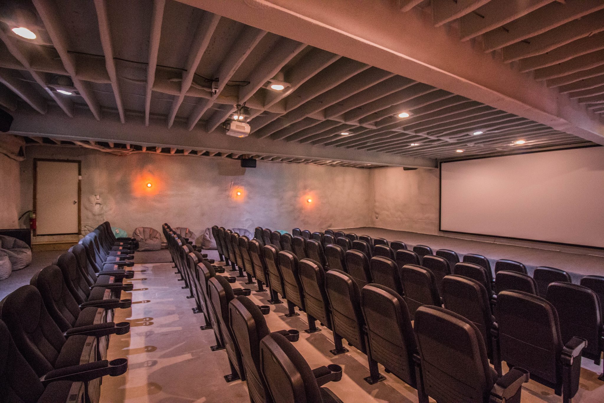 The theater: rows of dark seats rising towards a large screen with a low stage in front of it