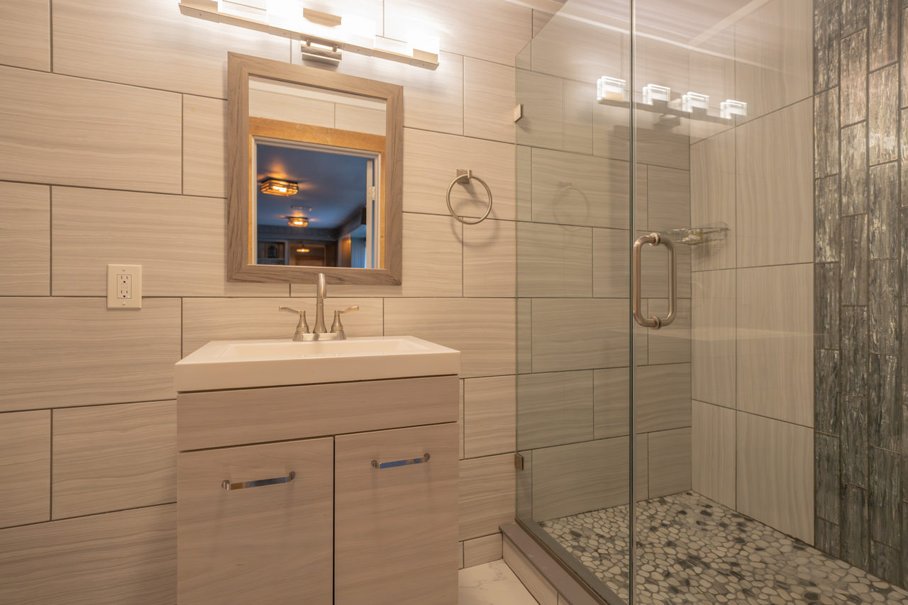 A bathroom tiled floor to ceiling in pale stone, with a glass shower and a pebbled floor