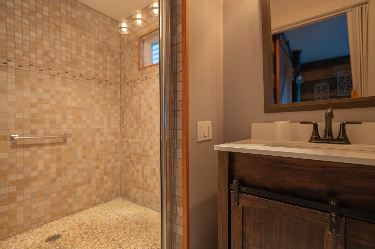 A bathroom with a mosaic-tiled walk-in shower behind glass and a dark timber vanity
