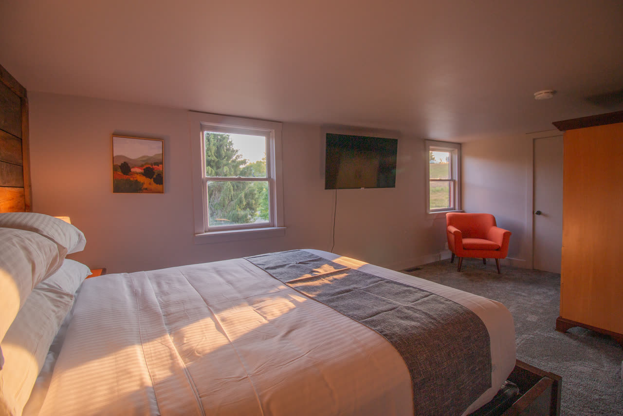 Bedroom 3, a queen bed in low evening light with a window onto the pines and an orange armchair in the corner