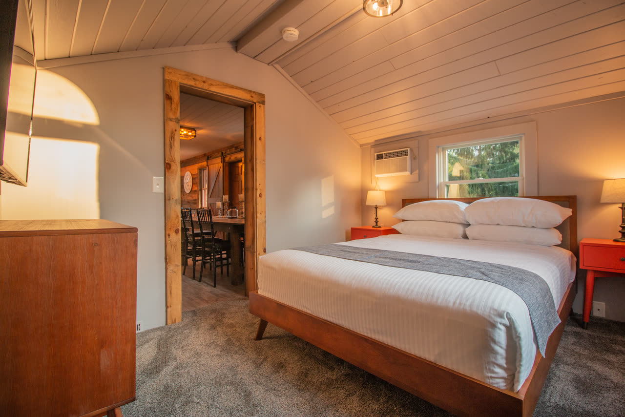 Bedroom 4, a queen bed under a sloped white ceiling, with the dining room through an open doorway