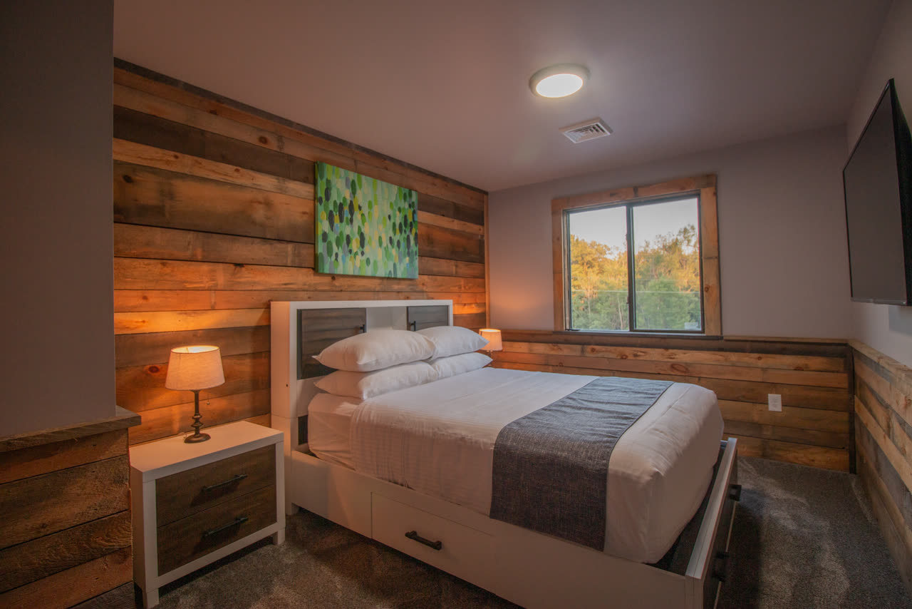 Bedroom 6, a queen bed against reclaimed timber, a green painting above it and a mirrored dresser opposite