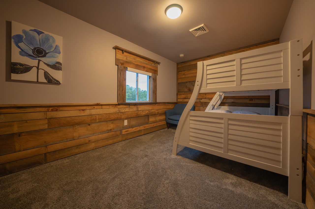 A bunk room with a twin bed over a full, against a wall of reclaimed timber boards