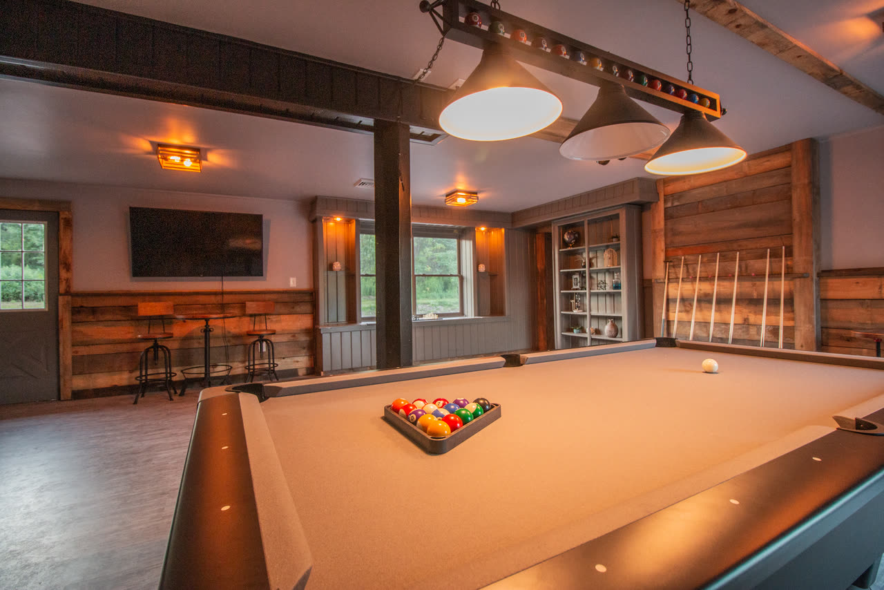 The bar and billiard room, reclaimed timber on the walls and a lit billiard table, with bar stools and a screen at the far end