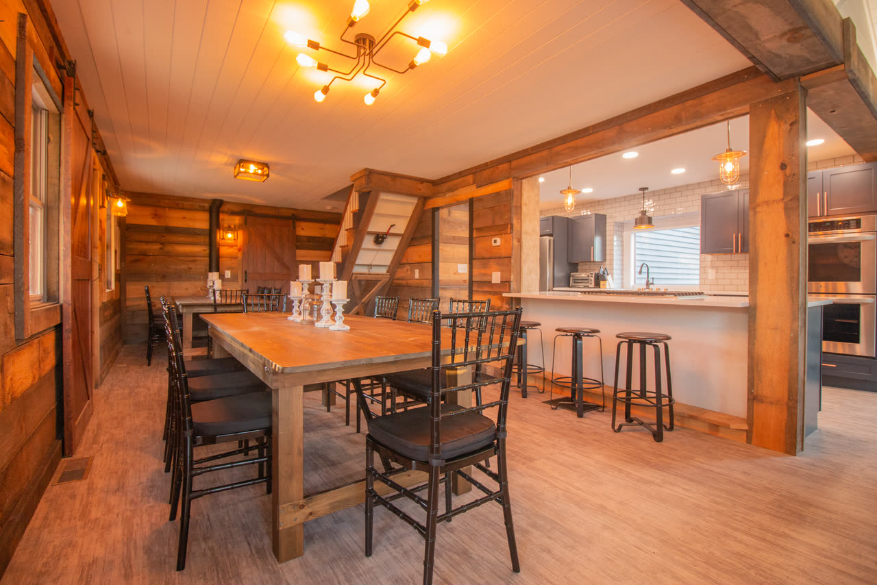 The dining room laid with two long tables and black chairs, the timber stair on one side and the living room fireplace through the opening beyond