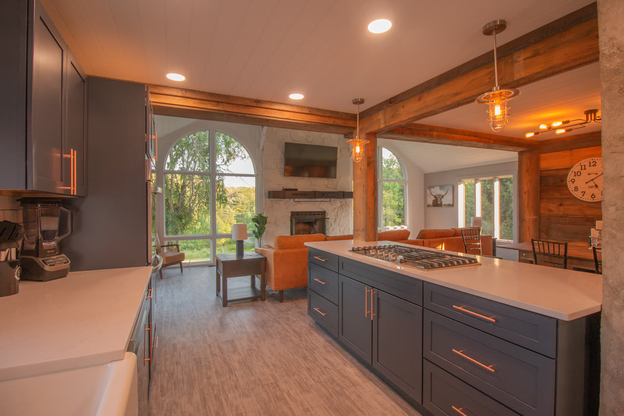 The kitchen, dark cabinets and a white farmhouse sink under a window, with double ovens beyond
