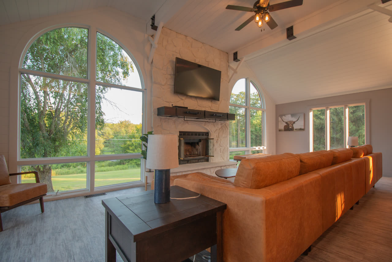 The living room, a stone fireplace between tall arched windows with a long leather sofa facing it