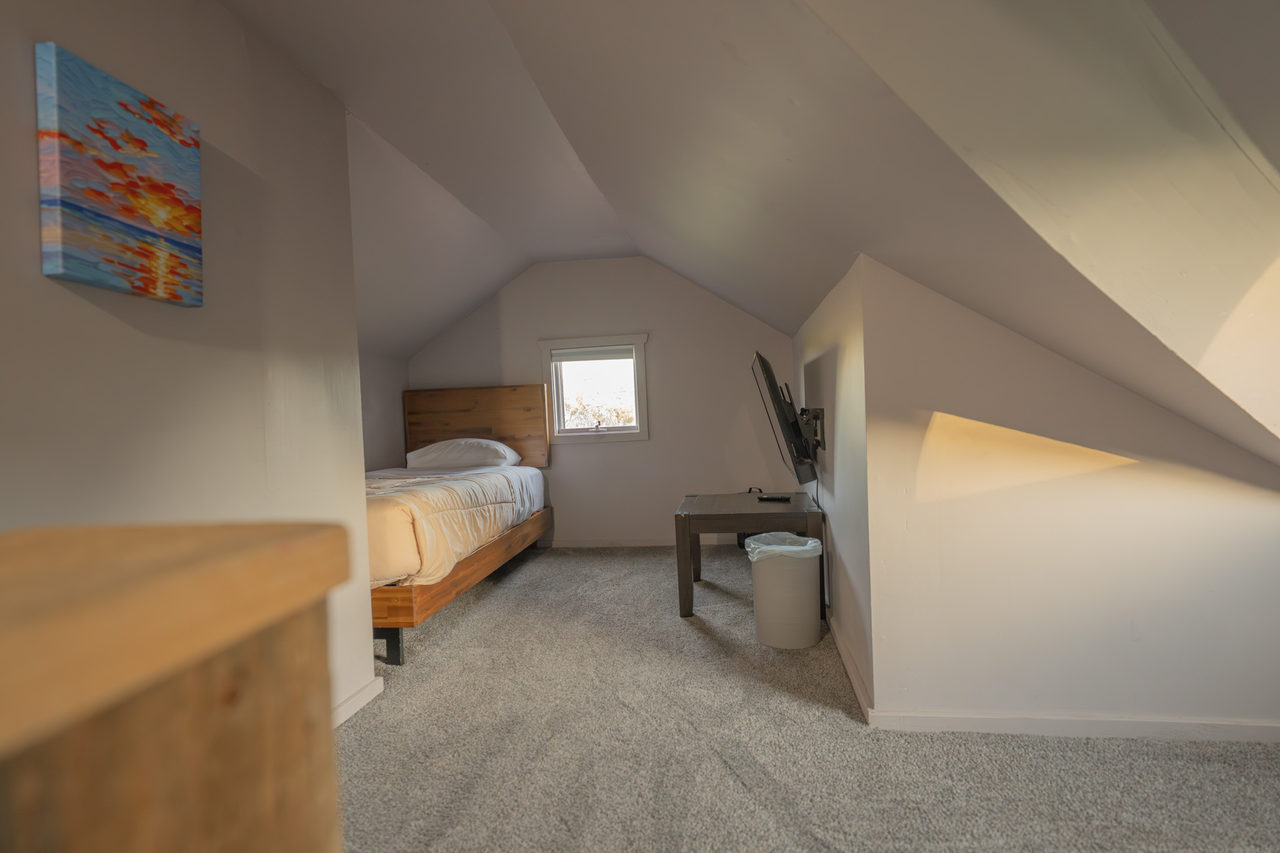 A twin bed under a sloping eave, with a small window at the gable end