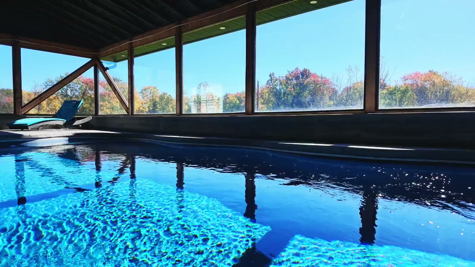 The Farmhouse's indoor pool on a bright autumn day, the water lit blue and the trees in fall color beyond a long wall of tall windows