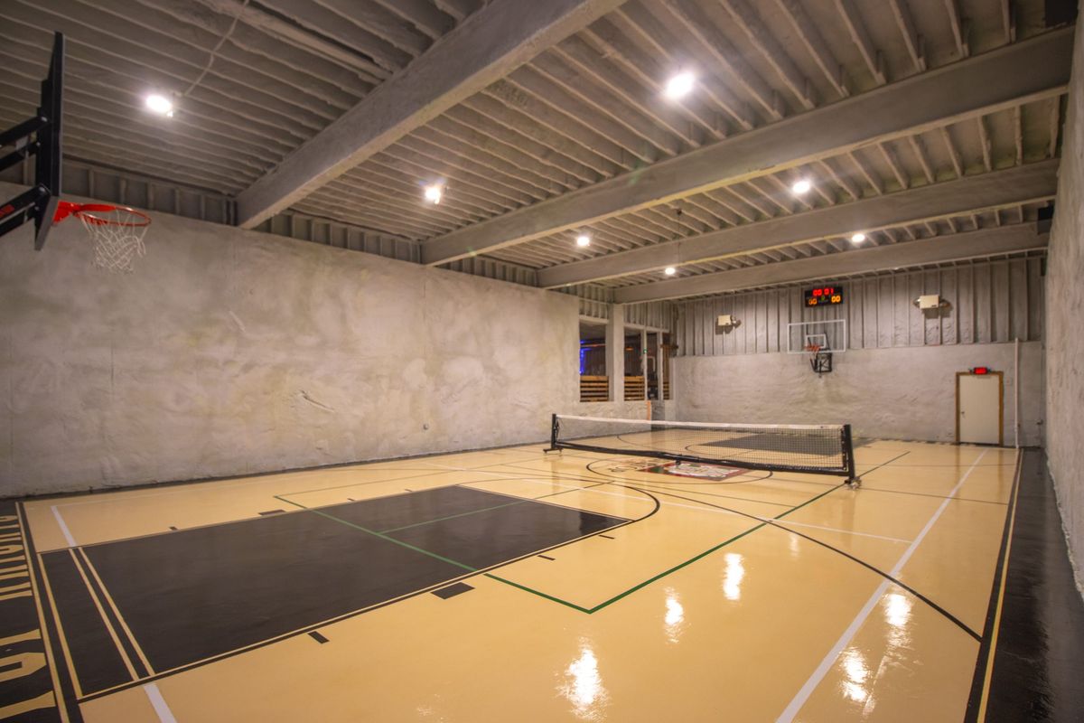 The indoor basketball court under bright lights, a pickleball net set up at centre court over painted lines