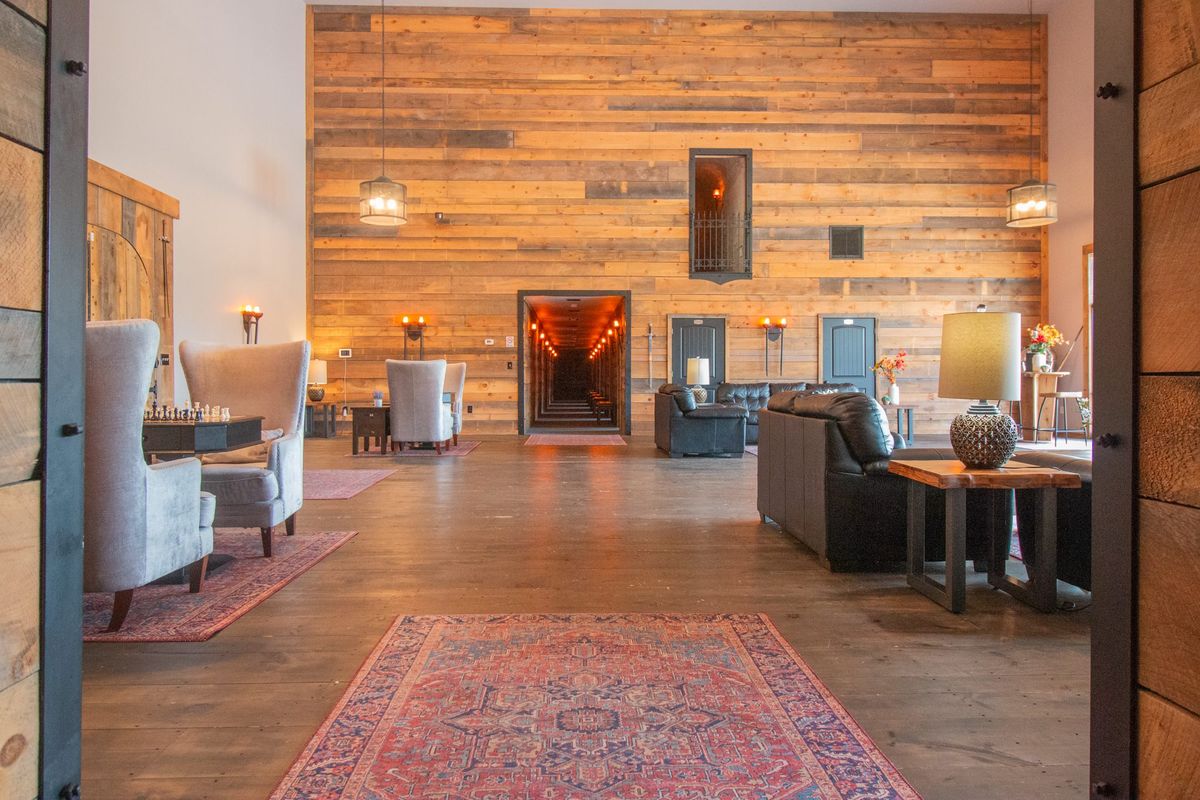 The Castle's foyer: timber-clad walls, armchairs and a rug, and a lit doorway through to the far side