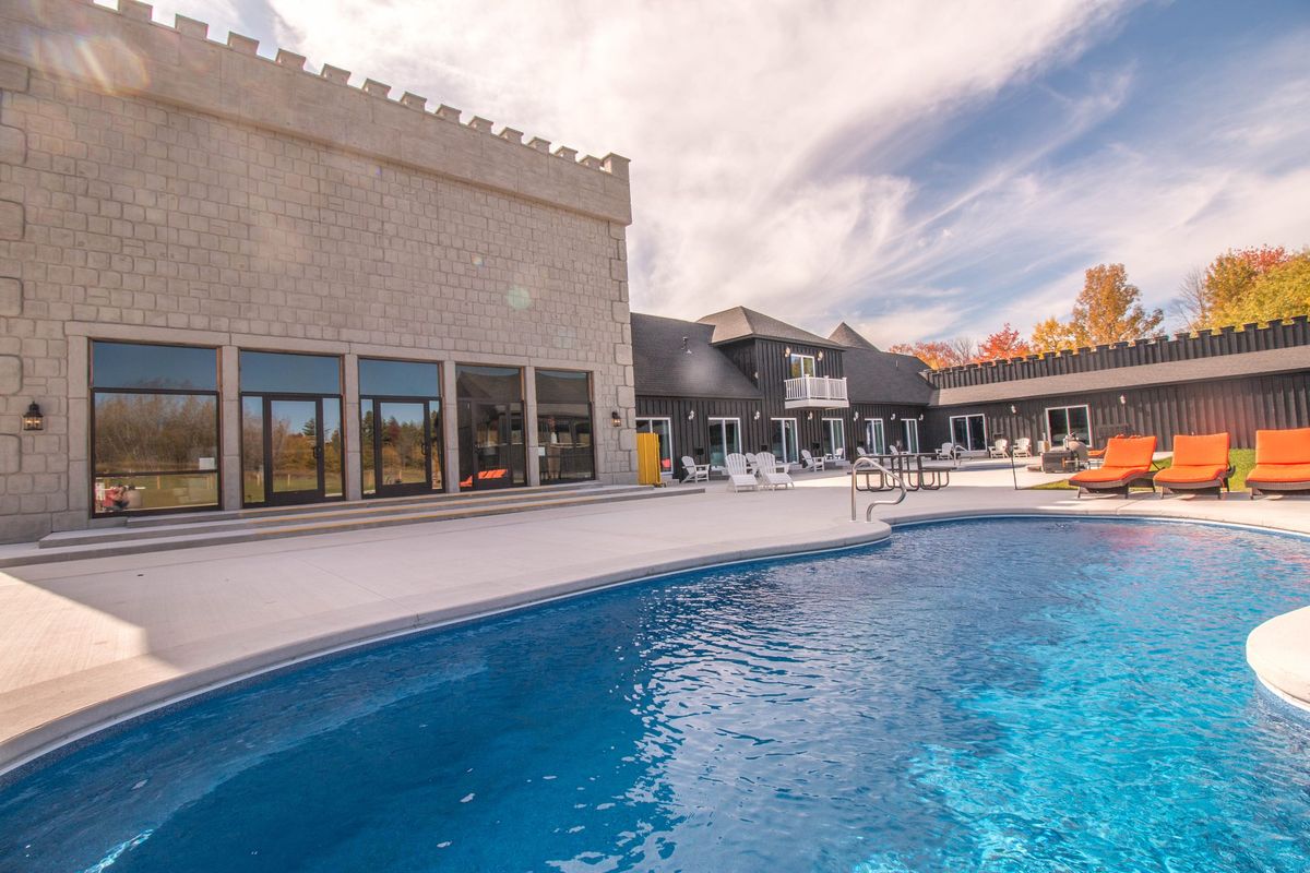 The Castle's outdoor pool beside a battlemented stone wall, orange loungers along the far side
