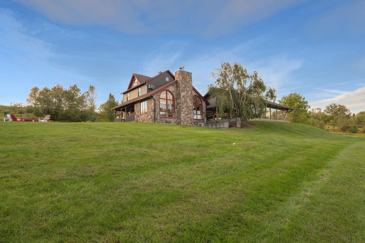 The Farmhouse from the back lawn under a blue sky: a stone gable with tall arched windows, and the glazed pool wing running low off it to the right