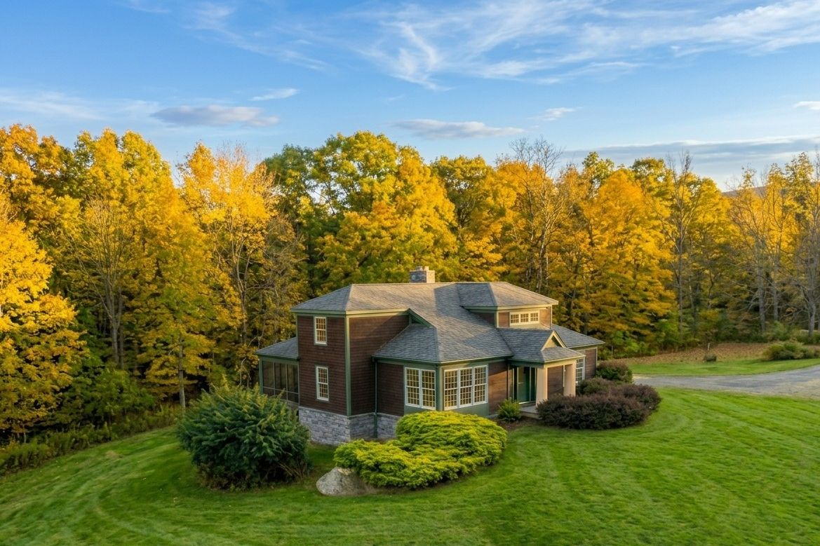 The Lodge from above in autumn under a blue sky, yellow maples behind it and a striped lawn around it