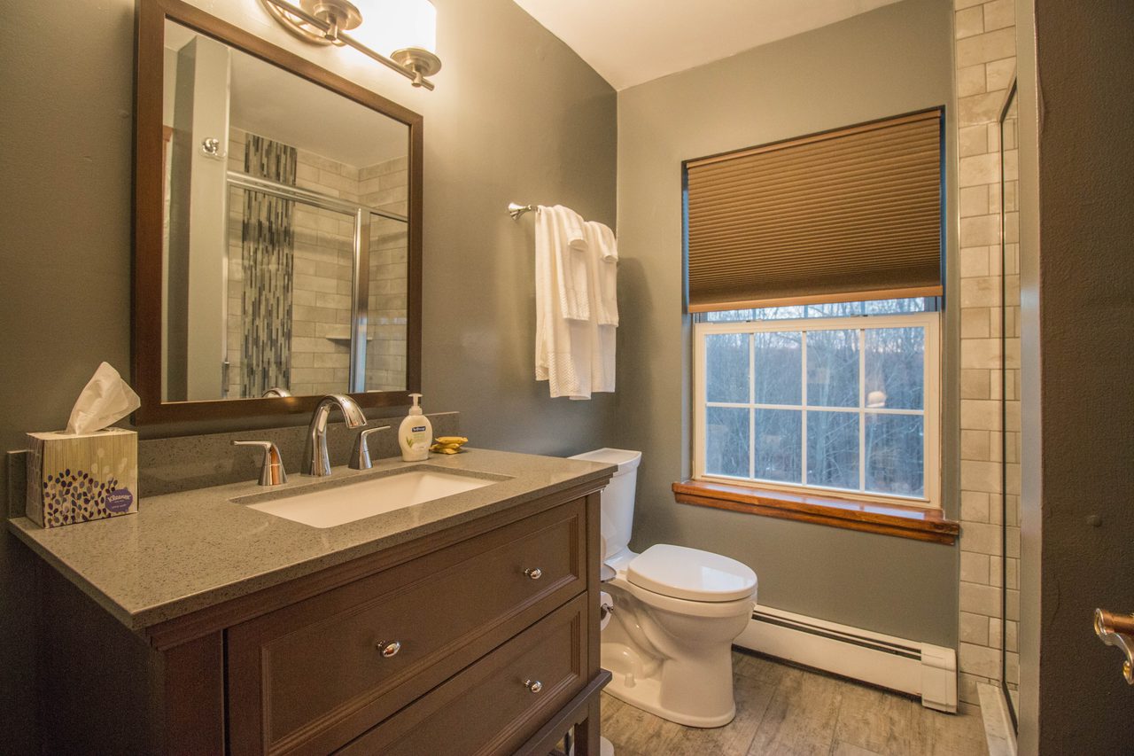 A bathroom with a dark vanity and a mirror, a window beside it
