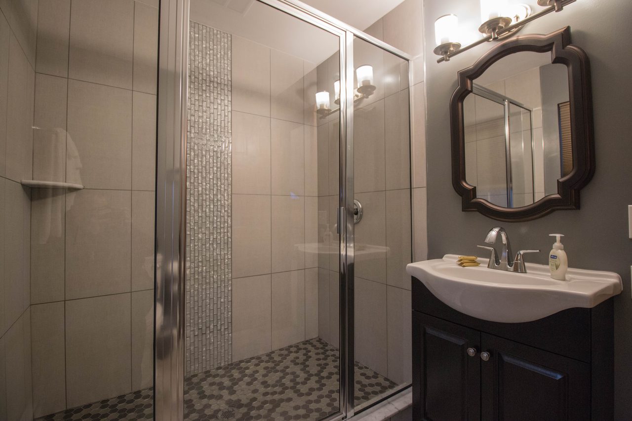 A bathroom with a glass shower and a tiled niche, towels on the rail