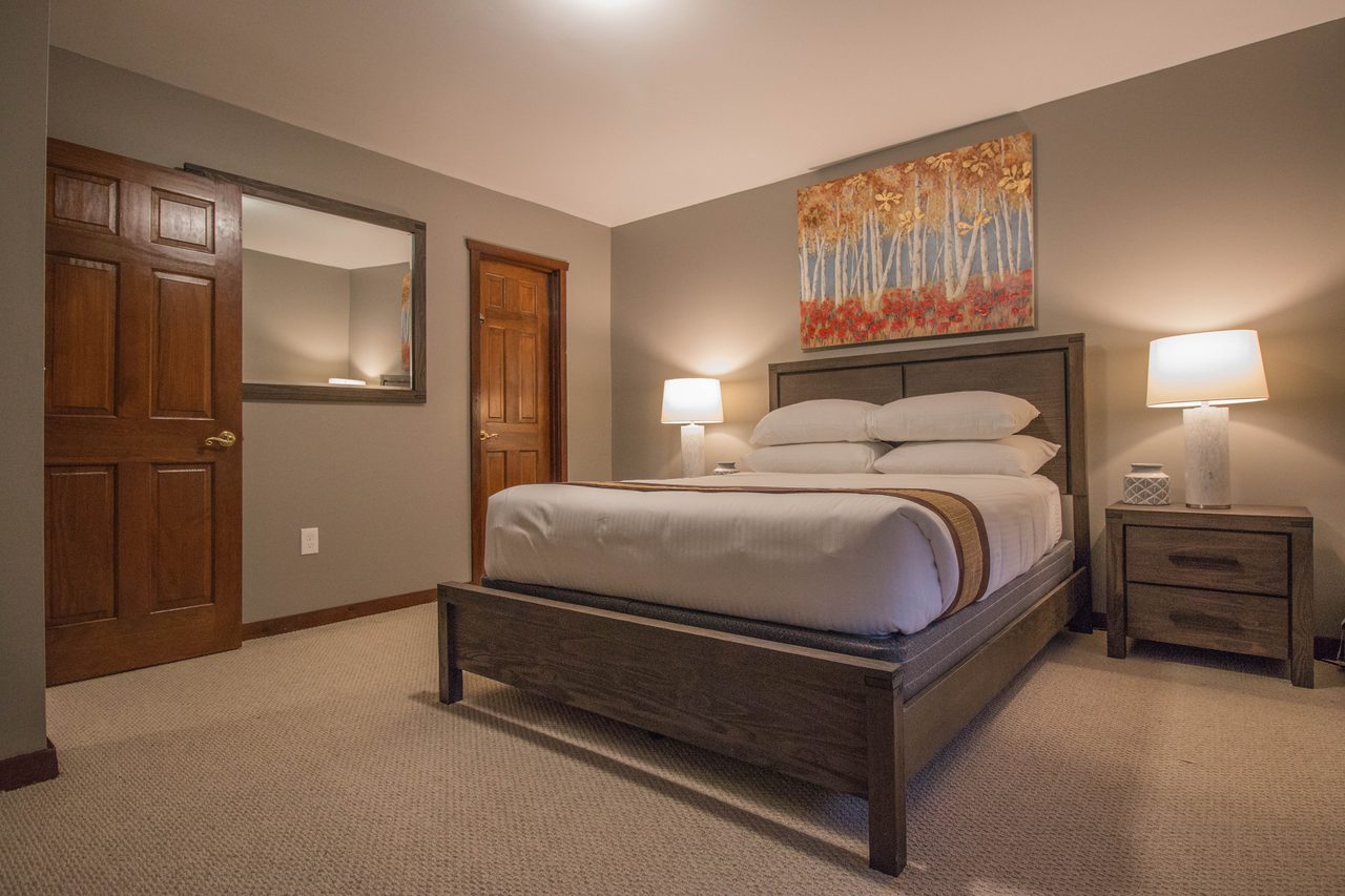 A bedroom with a queen bed under a framed print, a door through to the landing