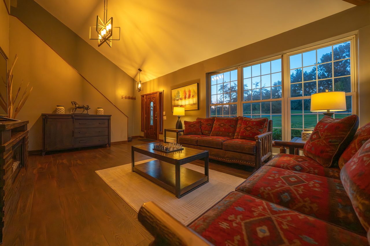 The great room seen from the dining end, sofas facing the windows and the stair rising on the right