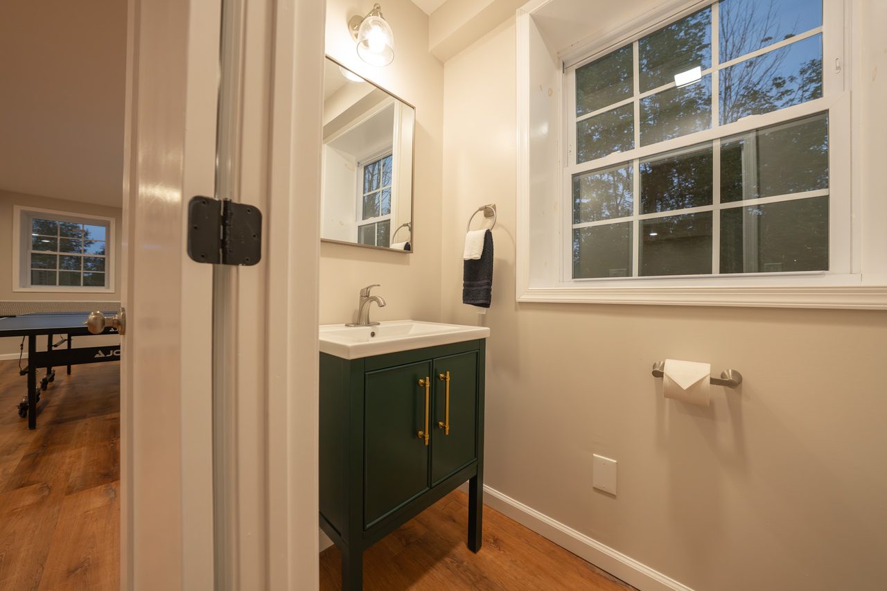 A half bath with a green vanity under a mirror, a window beside it