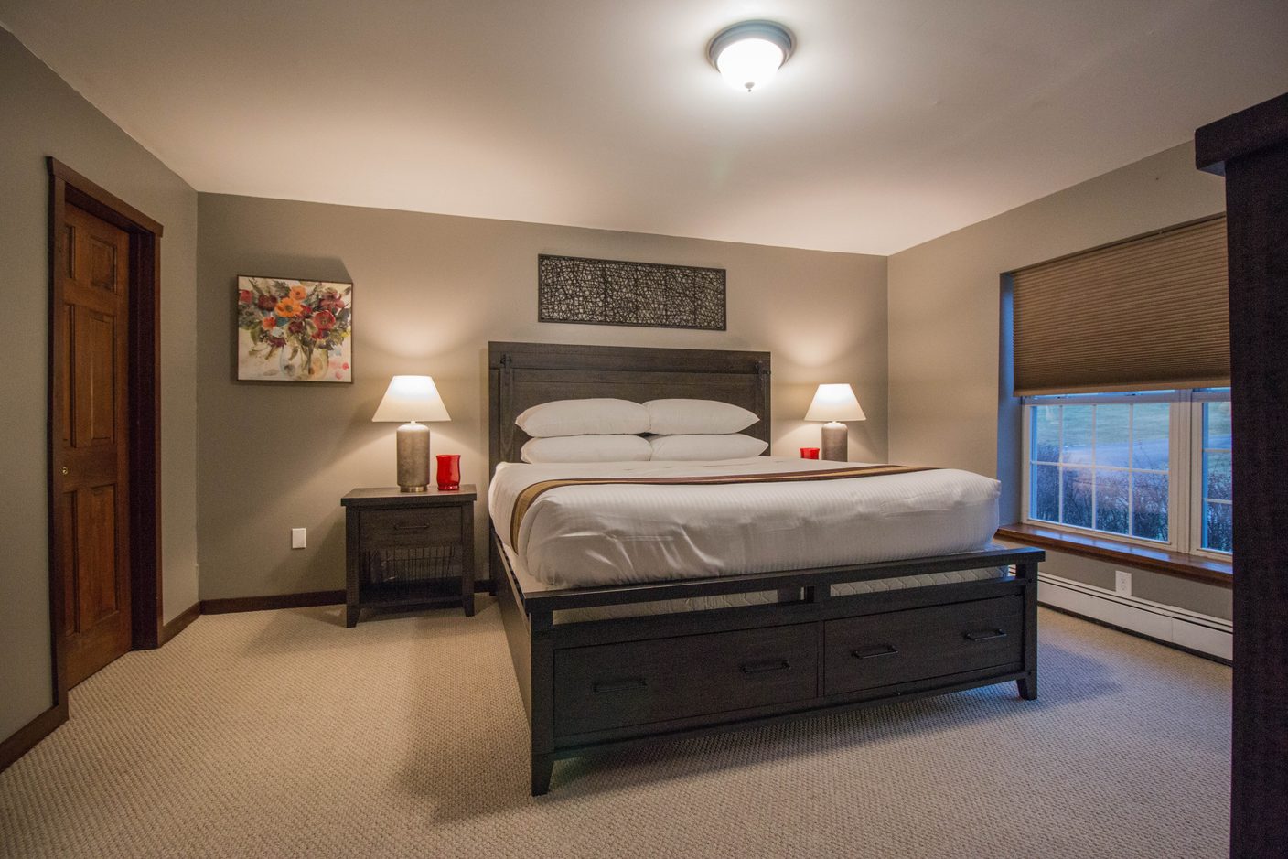 A bedroom with a king bed between two lamps and a window onto the fields