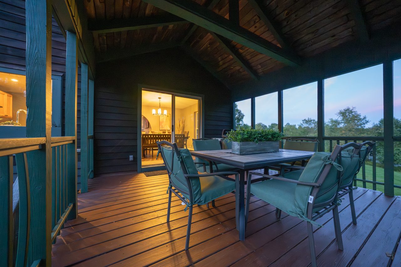 The screened porch at dusk, a table and chairs under the roof beams with the valley beyond the screens
