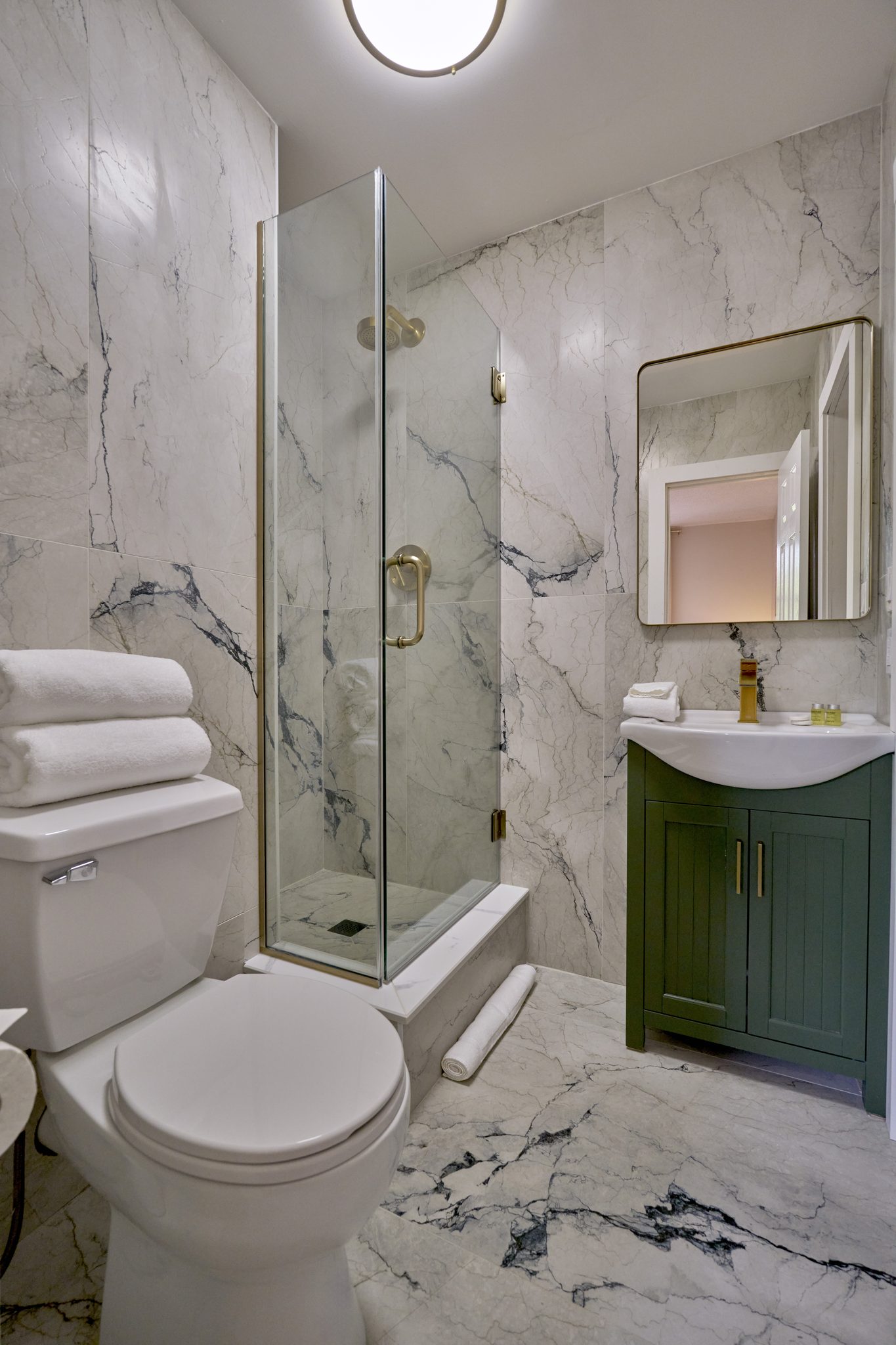 A bathroom with a glass shower, a dark vanity and white marble