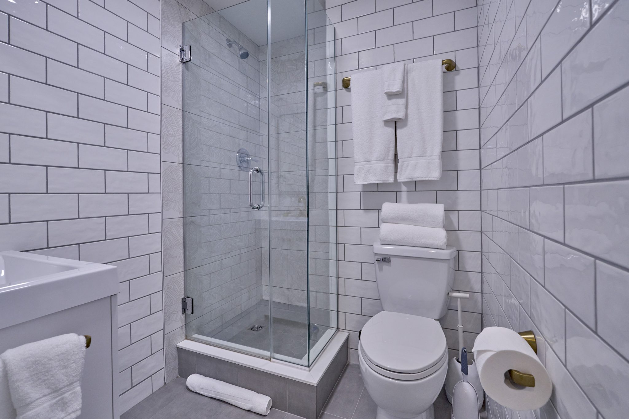 A bathroom in white subway tile with a glass corner shower and folded towels on a rail