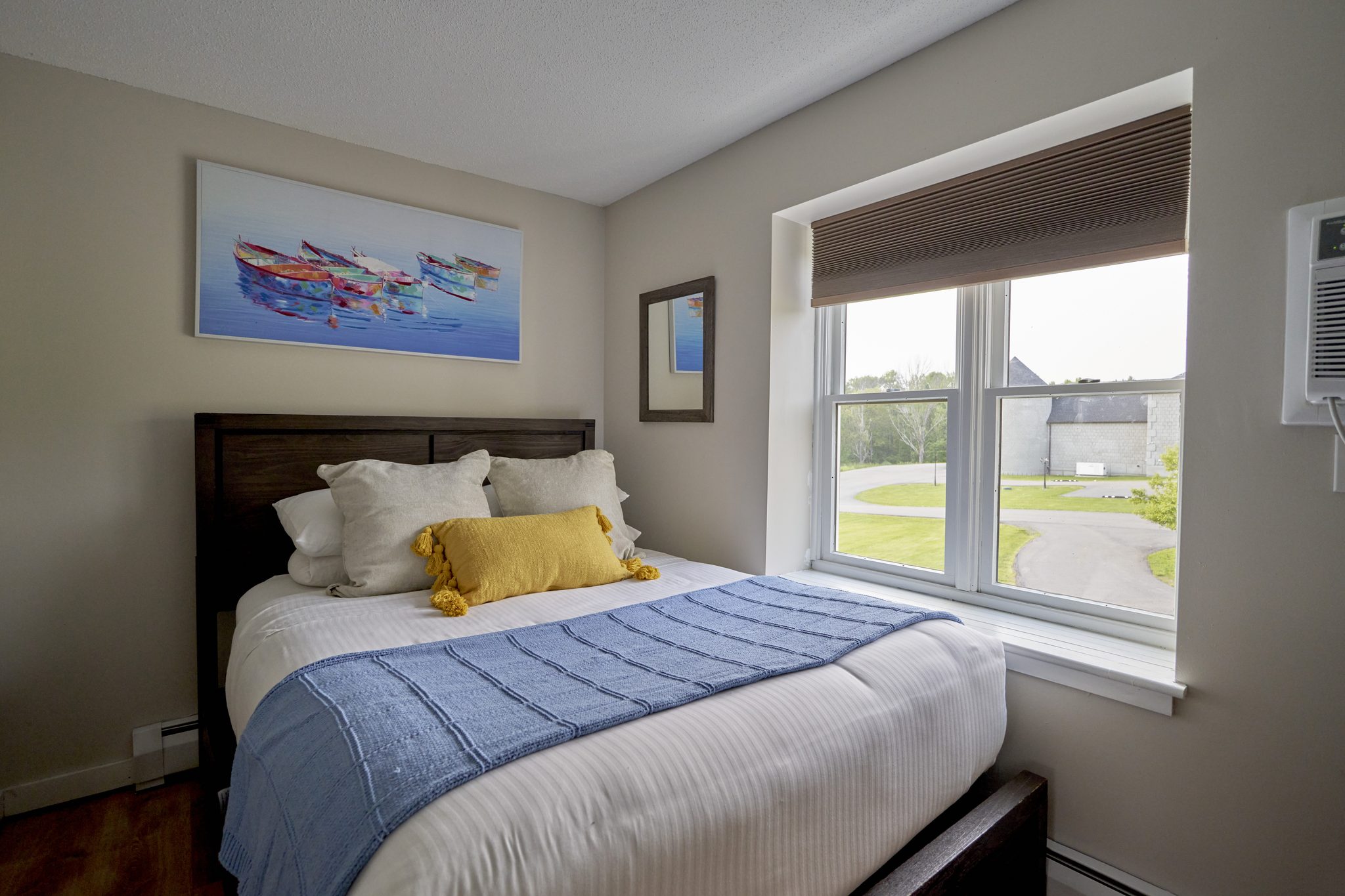 A queen bedroom with a three-pane window and a bright fish painting over the bed