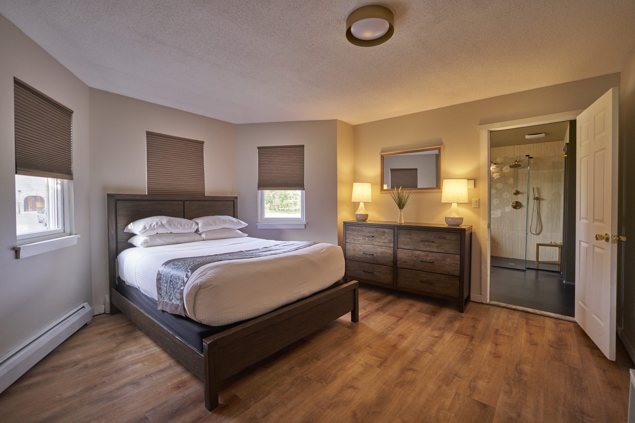 A queen bedroom with a dark dresser and an open door onto its own shower
