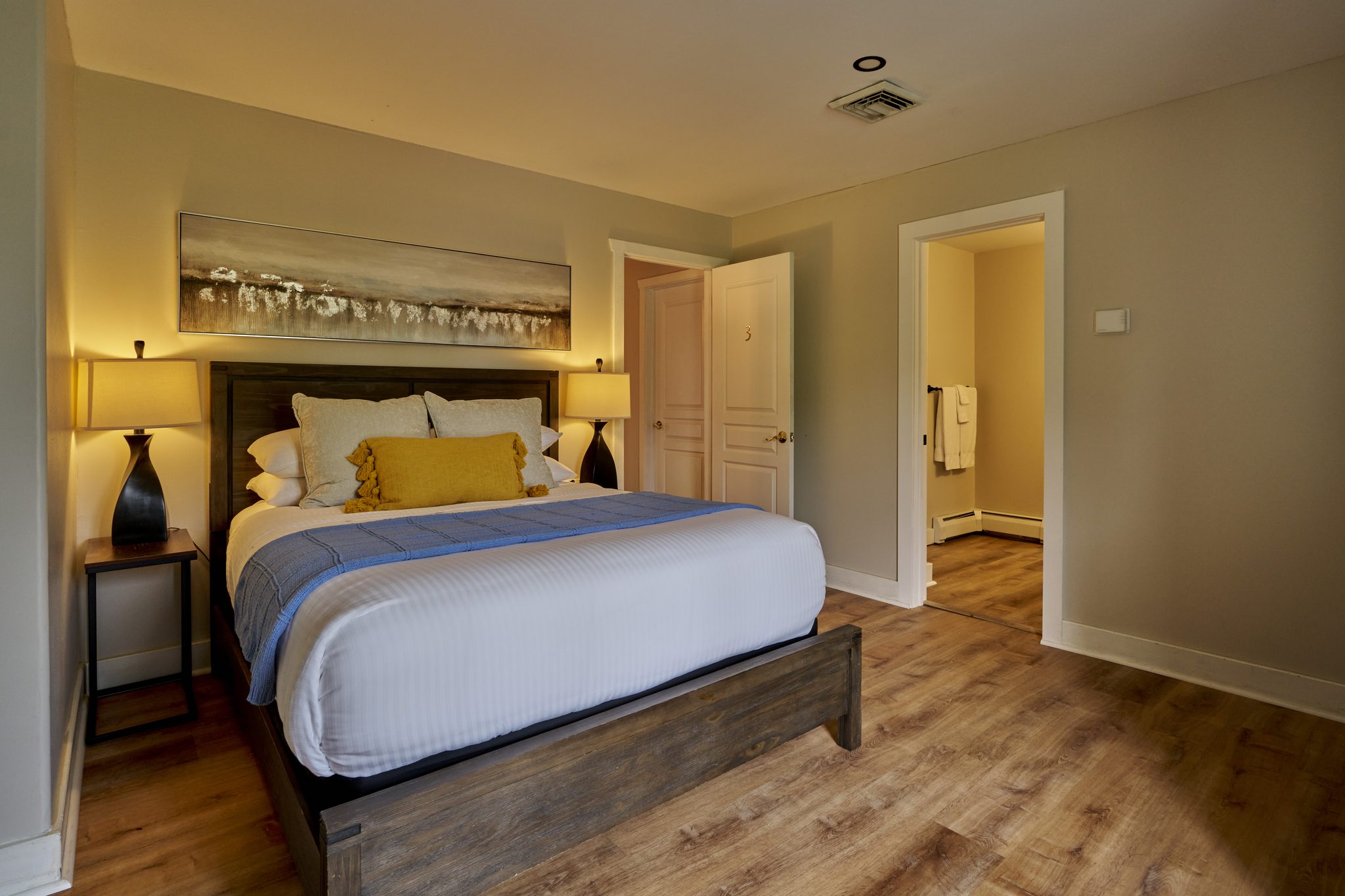 A queen bedroom with blue and yellow bedding against a grey headboard