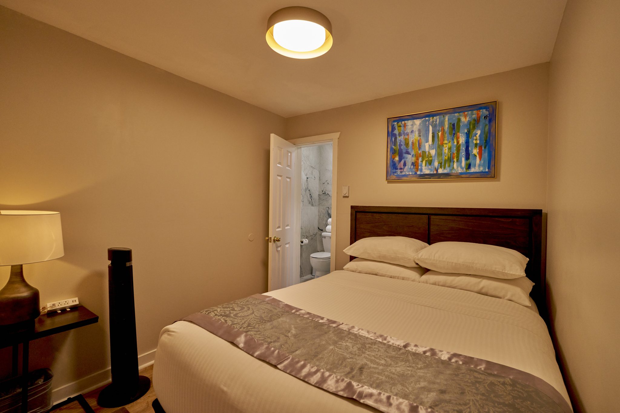 A queen bedroom with a gold satin runner across the bed and a door open to a bathroom