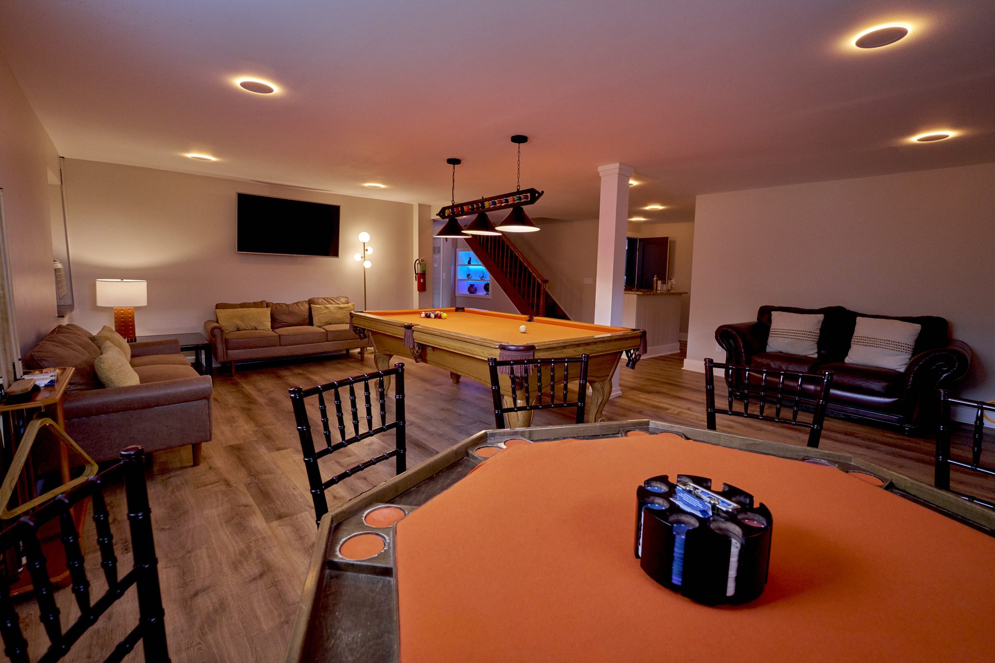 A basement room with a pool table under low pendant lights and a stone fireplace