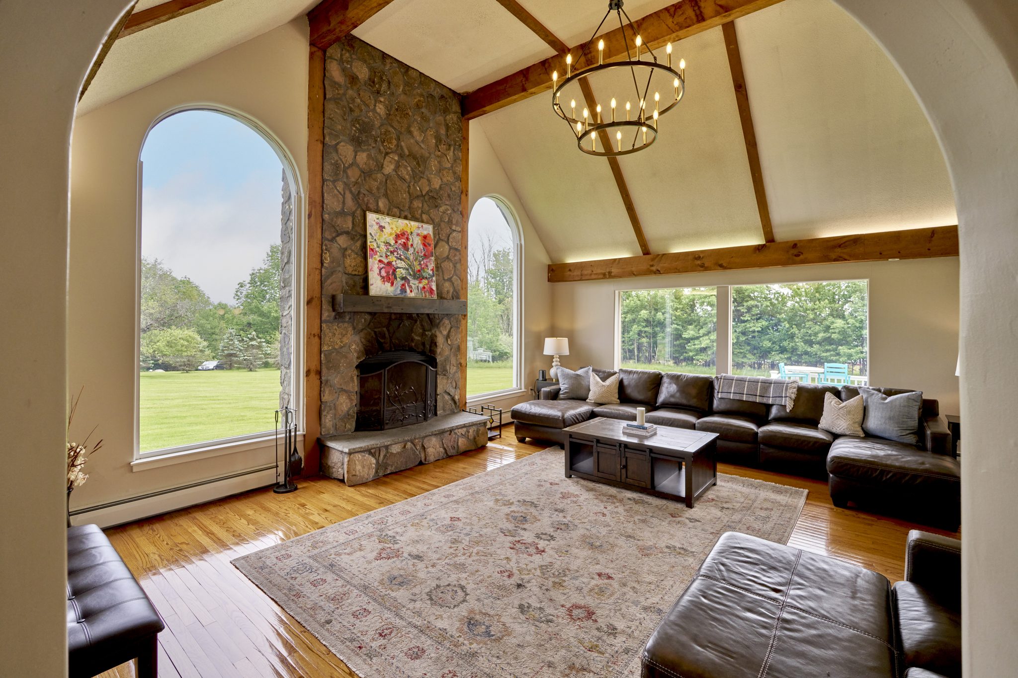 The Mansion's living room seen from the entry, a stone chimney between two arched windows under a vaulted timber ceiling