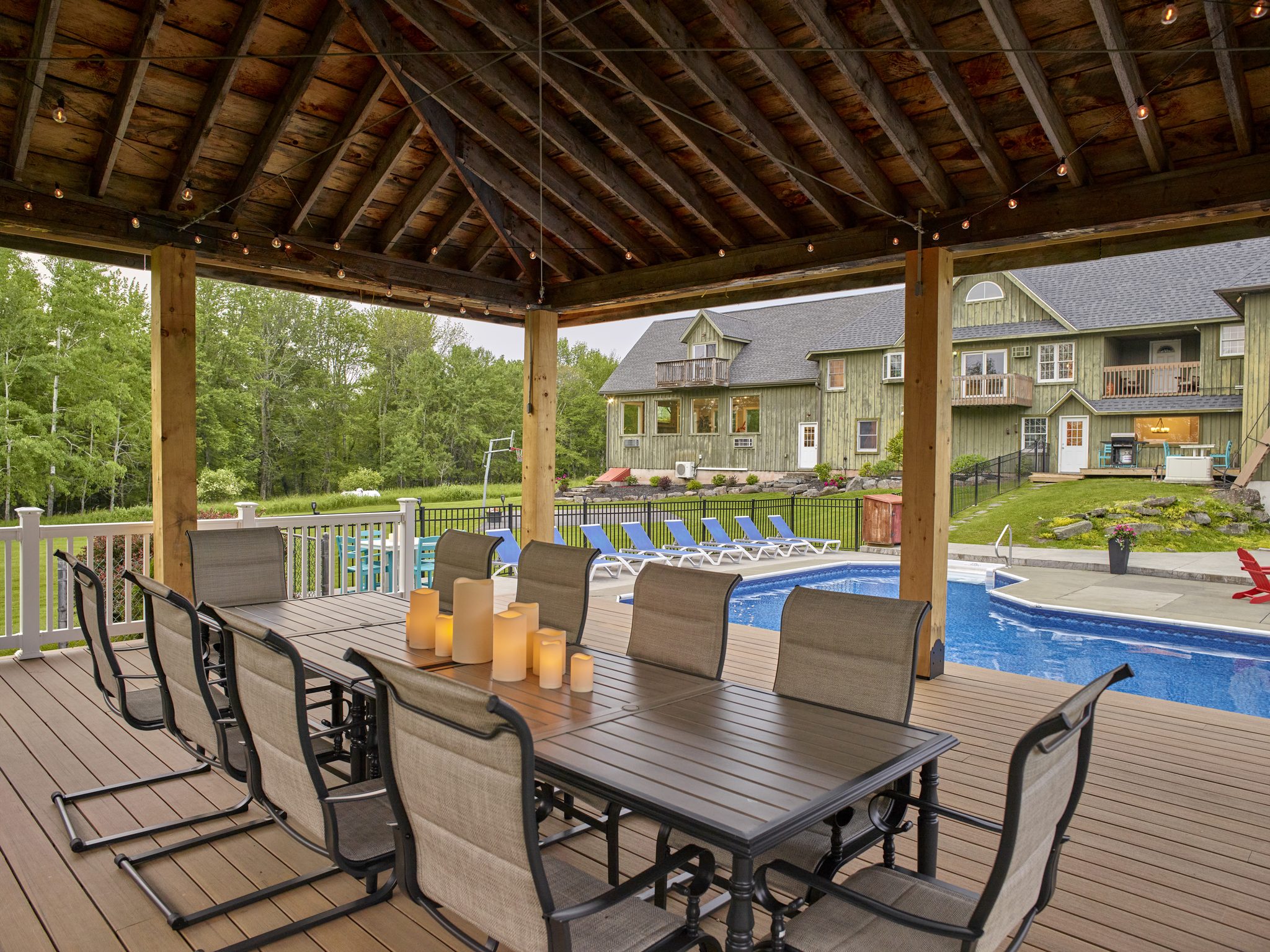 A covered timber gazebo with a long dining table, the pool and the Mansion behind it