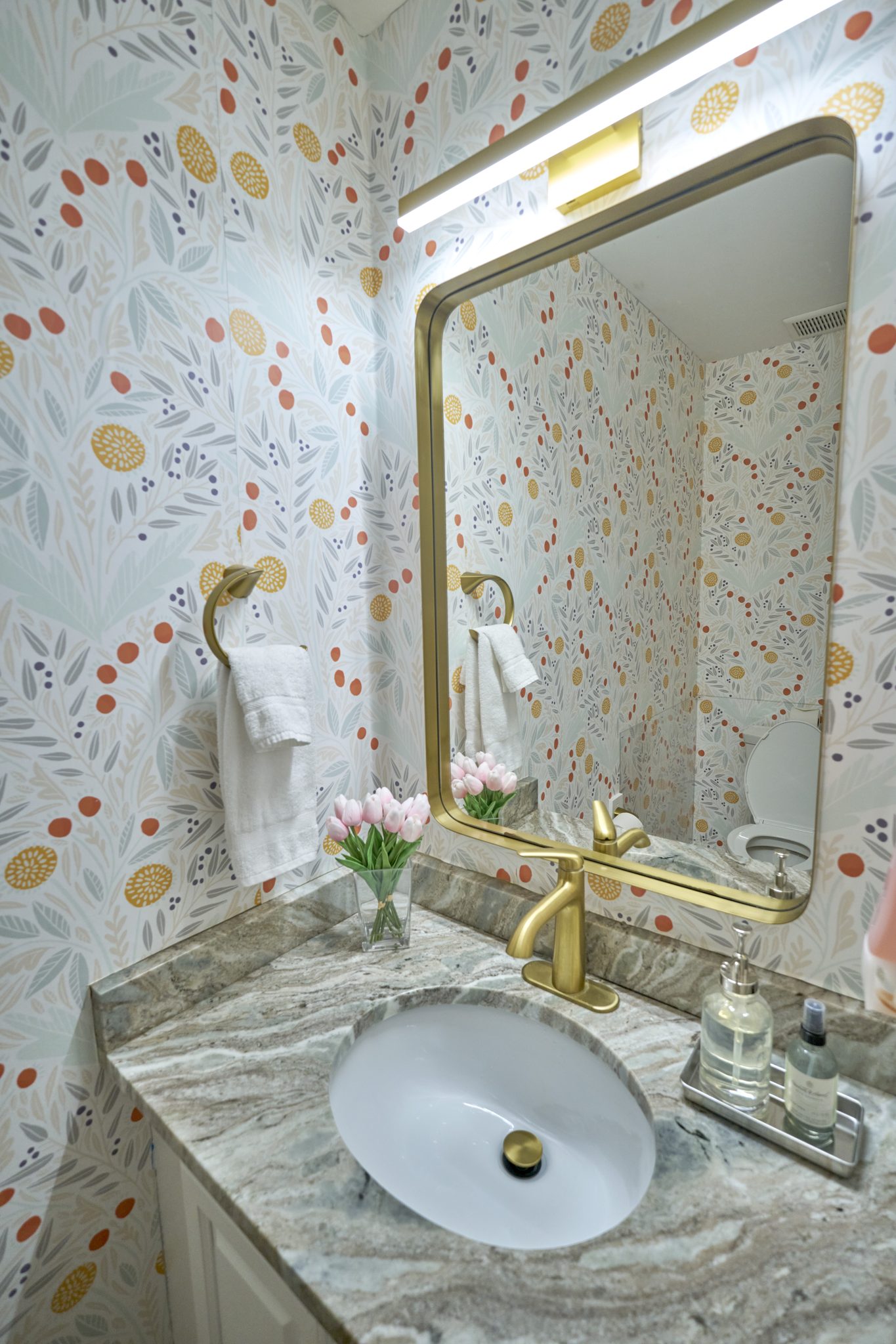 A half bath with a marble counter, patterned wallpaper and a gilt mirror