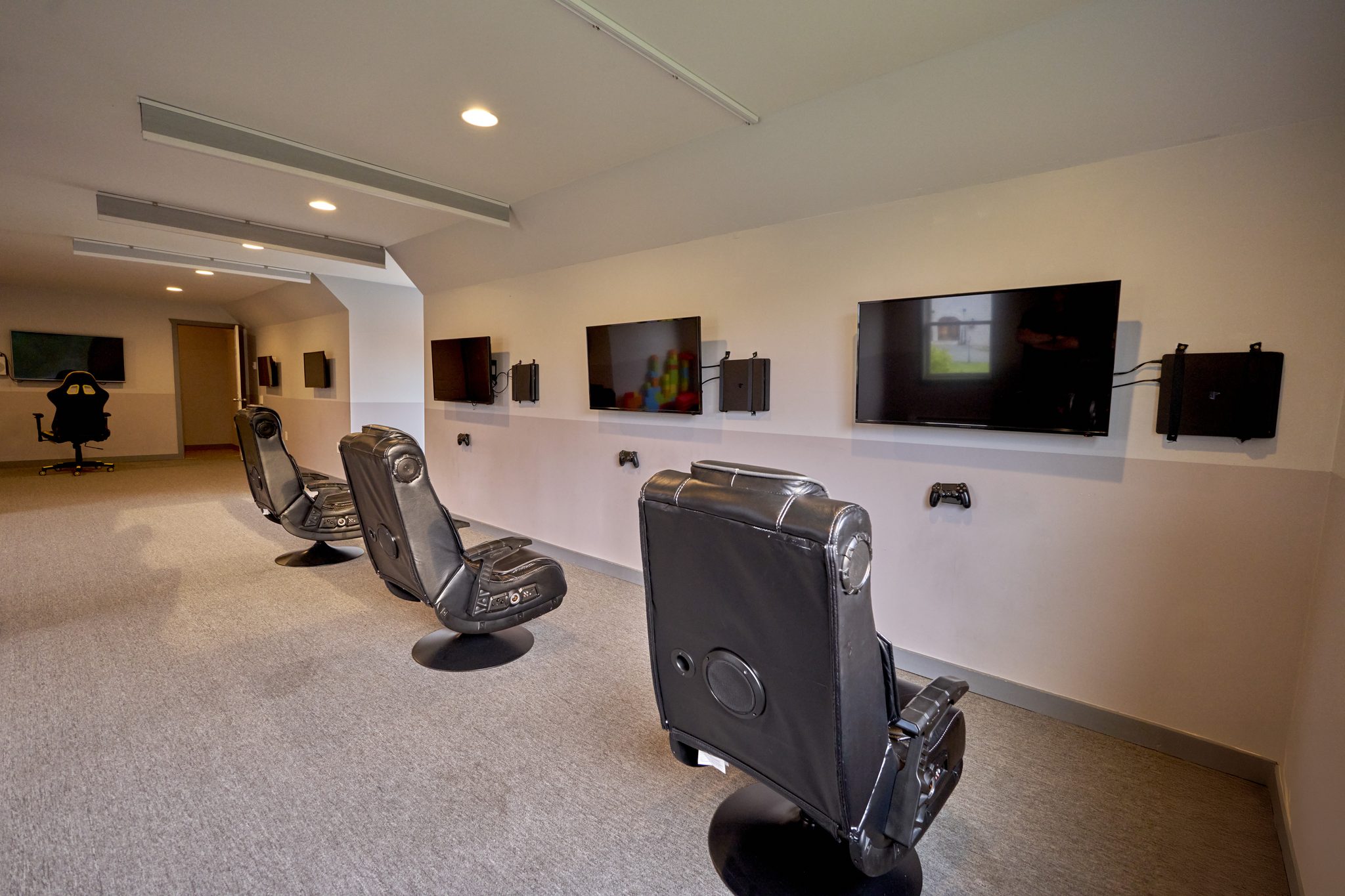 A long room with gaming chairs facing wall-mounted screens