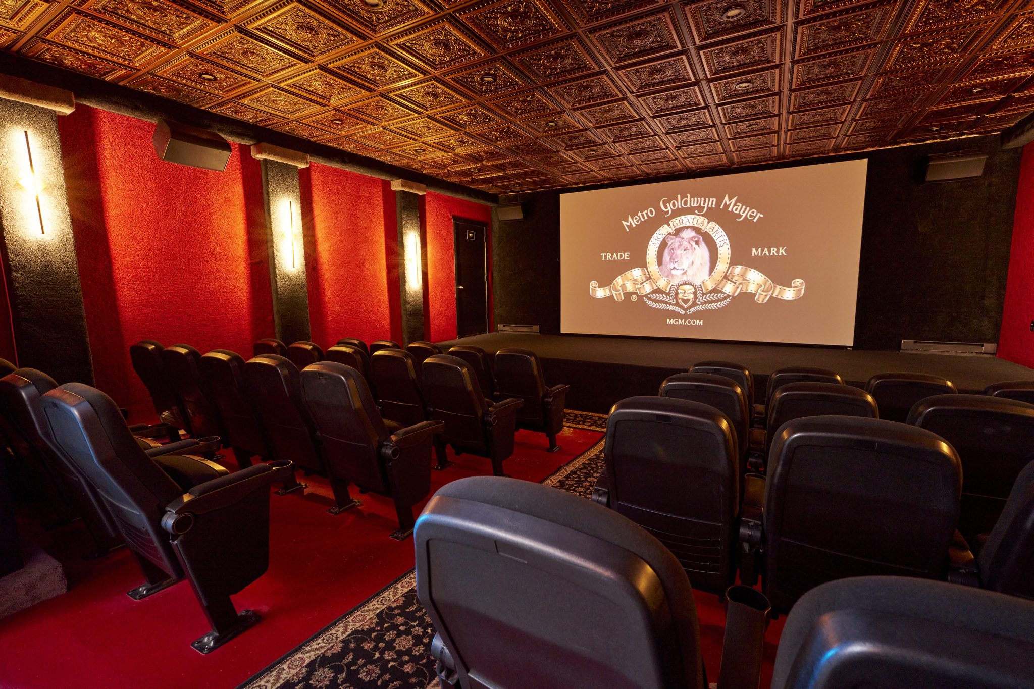 The Mansion's theater, red walls and a pressed tin ceiling above rows of recliners facing a screen