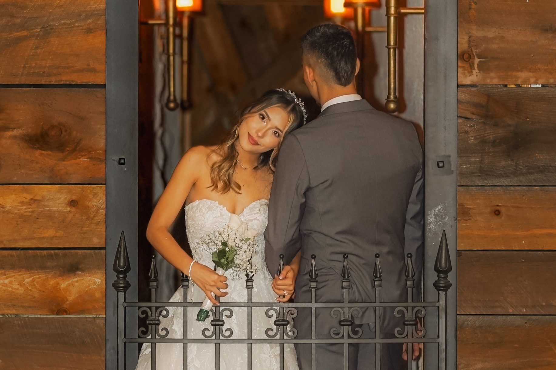 A bride and groom in a lit doorway at the Castle, framed by an ornamental iron gate, with reclaimed timber walls either side